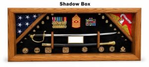 Shadow box military display case featuring a folded U.S. flag, U.S. Marine Corps flag, ceremonial sword, medals, ribbons, rank insignia, challenge coins, and a blank nameplate in an oak wood frame on a white background labeled "Shadow Box".